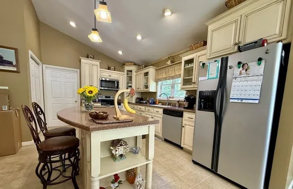 a kitchen with stainless steel appliances kitchen island granite countertop a refrigerator a sink dishwasher a stove a dining table and chairs with wooden floor