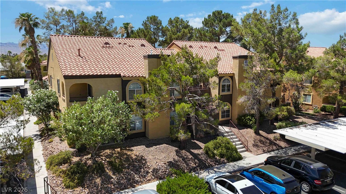 7950 West Flamingo Road, Unit 1180 Las Vegas, NV 89147 - Photo 1 of 26 Mediterranean-inspired multi-family complex featuring stucco walls and terracotta roof tiles, nestled among mature trees and desert landscaping.