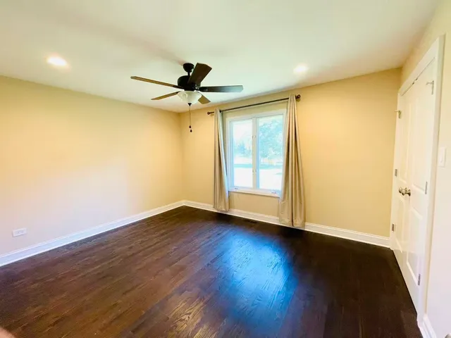 a view of an empty room with wooden floor and a ceiling fan