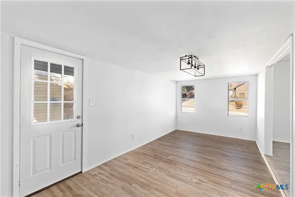 an empty room with wooden floor chandelier and windows