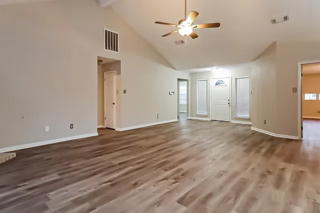 a view of an empty room with chandelier fan and wooden floor