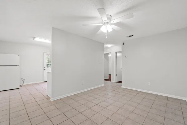 an empty room with fan and way to kitchen