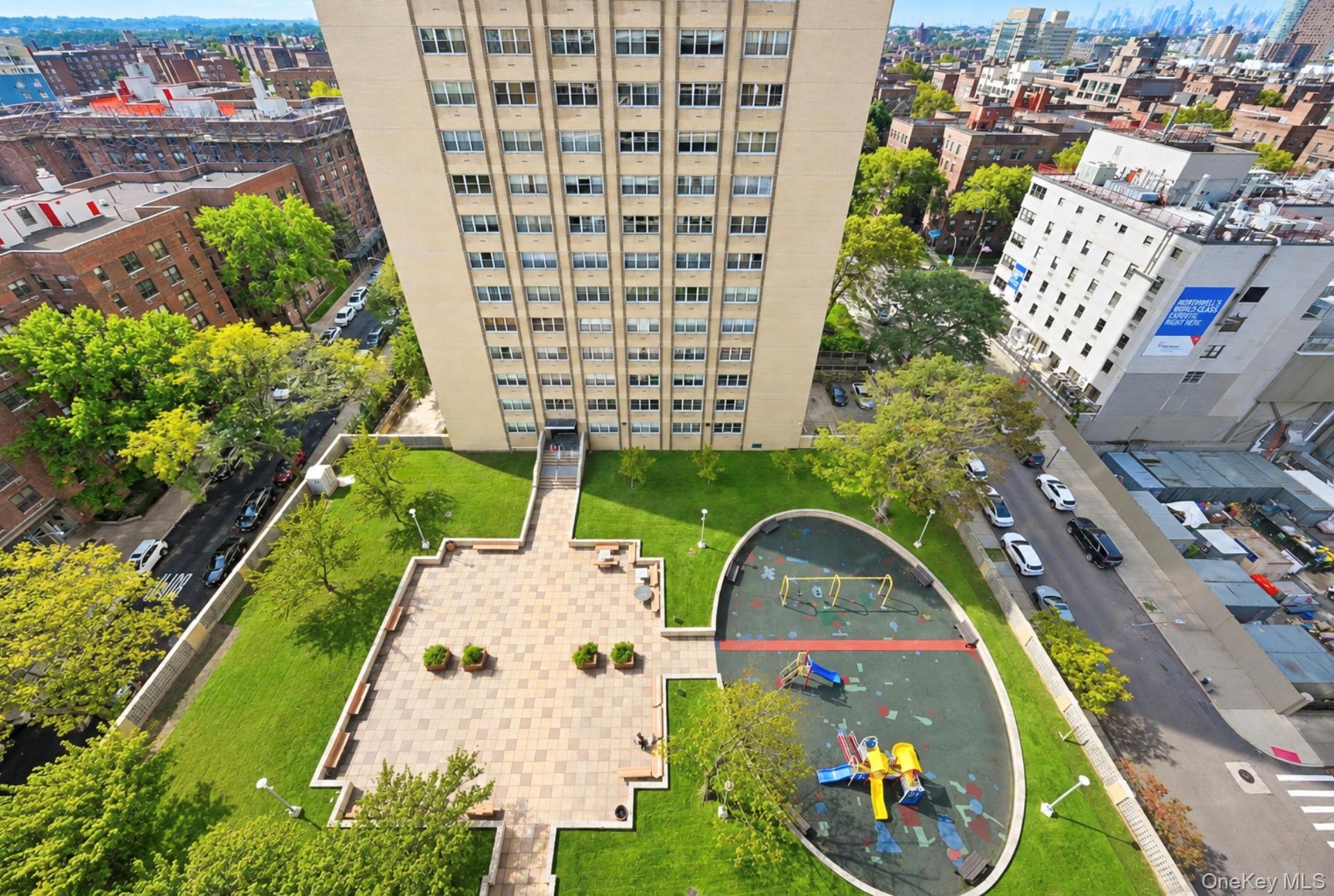 102-30 66th Road, Unit 17E Queens, NY 11375 - Photo 3 of 21 Expansive green space featuring a paved patio area, manicured lawn, and a dedicated play area