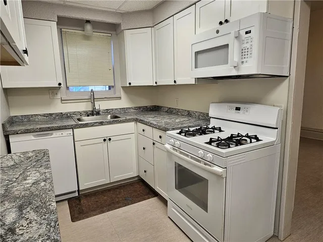 a white kitchen with stainless steel appliances granite countertop a stove a sink and a microwave