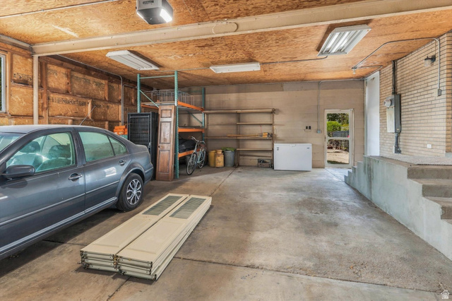15295 North 5400th Street West Riverside, UT 84334 - Photo 38 of 54 Concrete flooring in garage featuring exposed wood ceiling, fluorescent lighting, and a utility door
