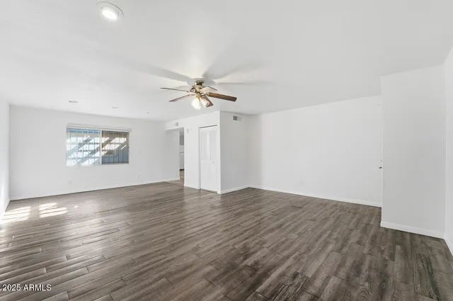 an empty room with wooden floor ceiling fan and windows