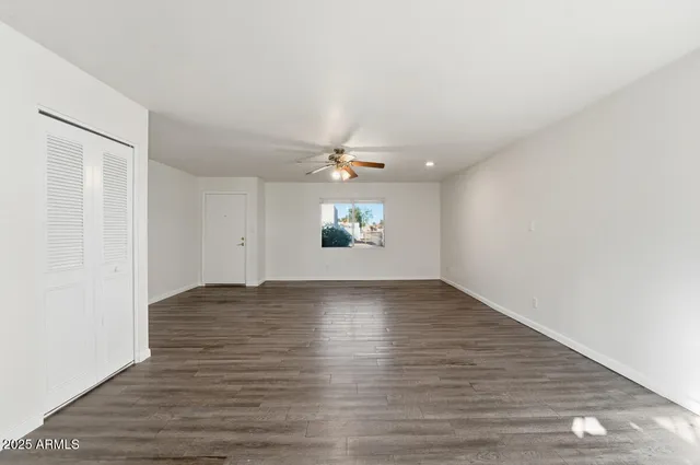 an empty room with wooden floor chandelier fan and windows