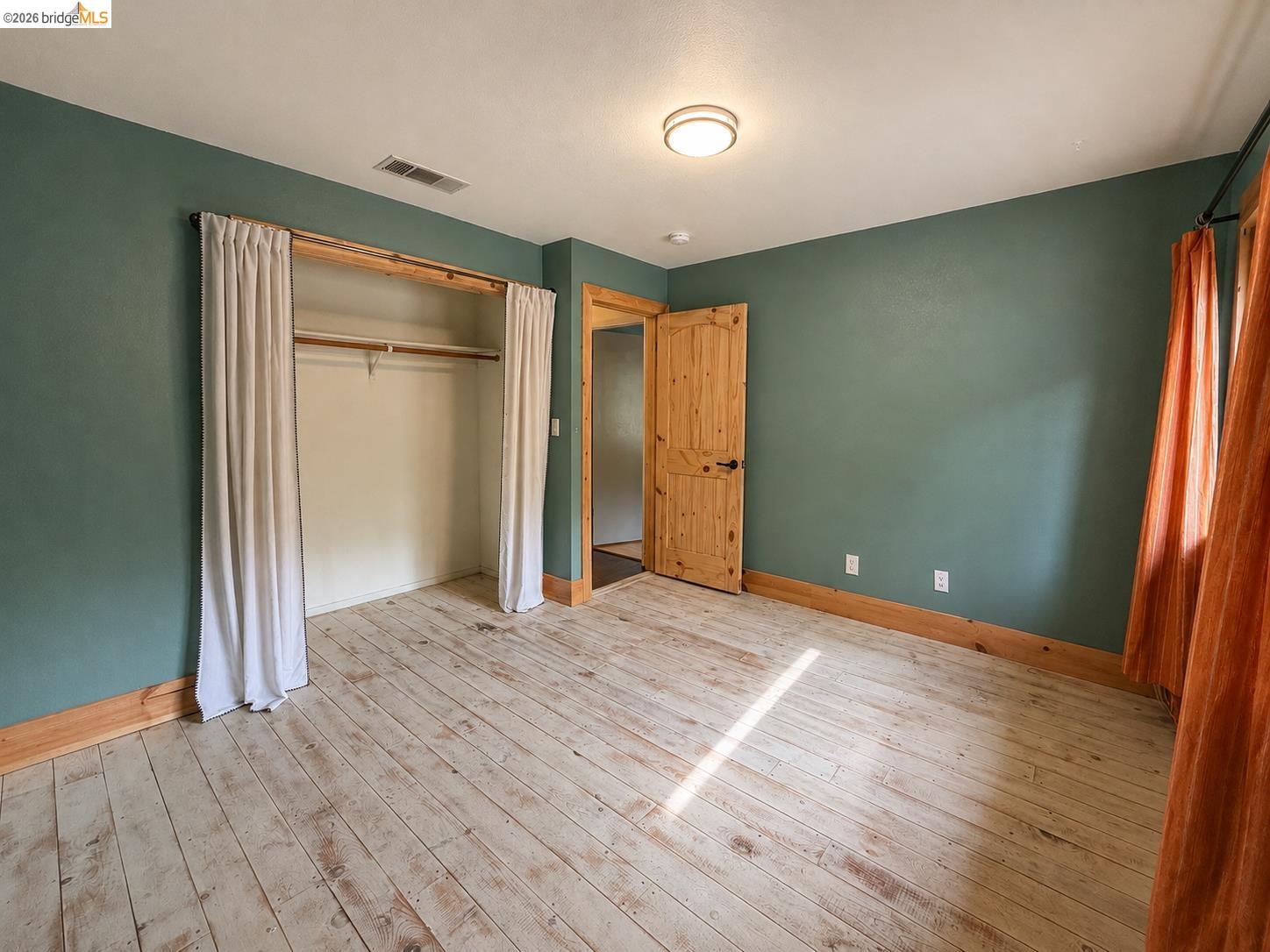 20663 Ferretti Road Groveland, CA 95321 - Photo 28 of 41 Wood-finish flooring, deep green wall color, natural wood trim, interior wood door with black hardware, and an overhead flush-mount light fixture