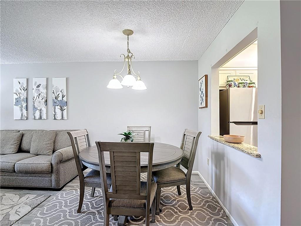 200 Turtle Lake Court, Unit 109 Naples, FL 34105 - Photo 11 of 37 Dining space with a textured ceiling, a chandelier, and wood finished floors