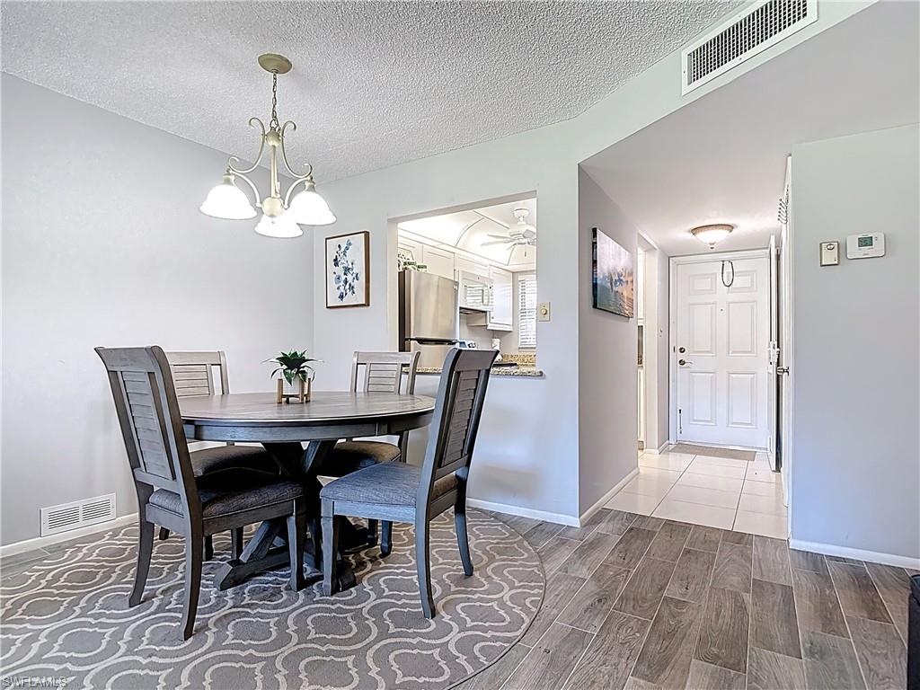 200 Turtle Lake Court, Unit 109 Naples, FL 34105 - Photo 13 of 37 Dining space featuring wood finish floors, a textured ceiling, and a chandelier