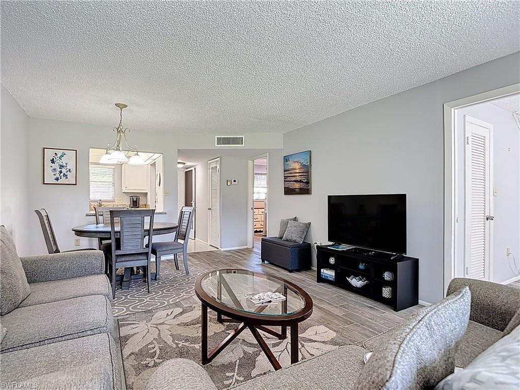200 Turtle Lake Court, Unit 109 Naples, FL 34105 - Photo 19 of 37 Living room featuring wood finished floors, a textured ceiling, and a chandelier