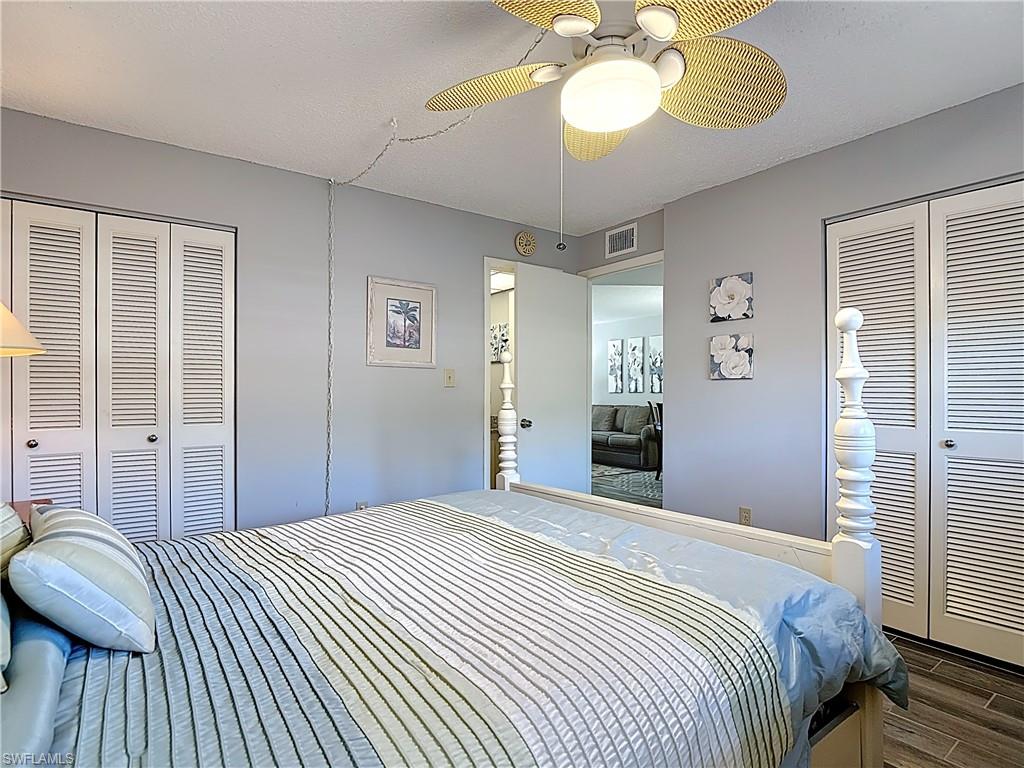 200 Turtle Lake Court, Unit 109 Naples, FL 34105 - Photo 23 of 37 Bedroom featuring a ceiling fan, wood finished floors, a textured ceiling, and two closets