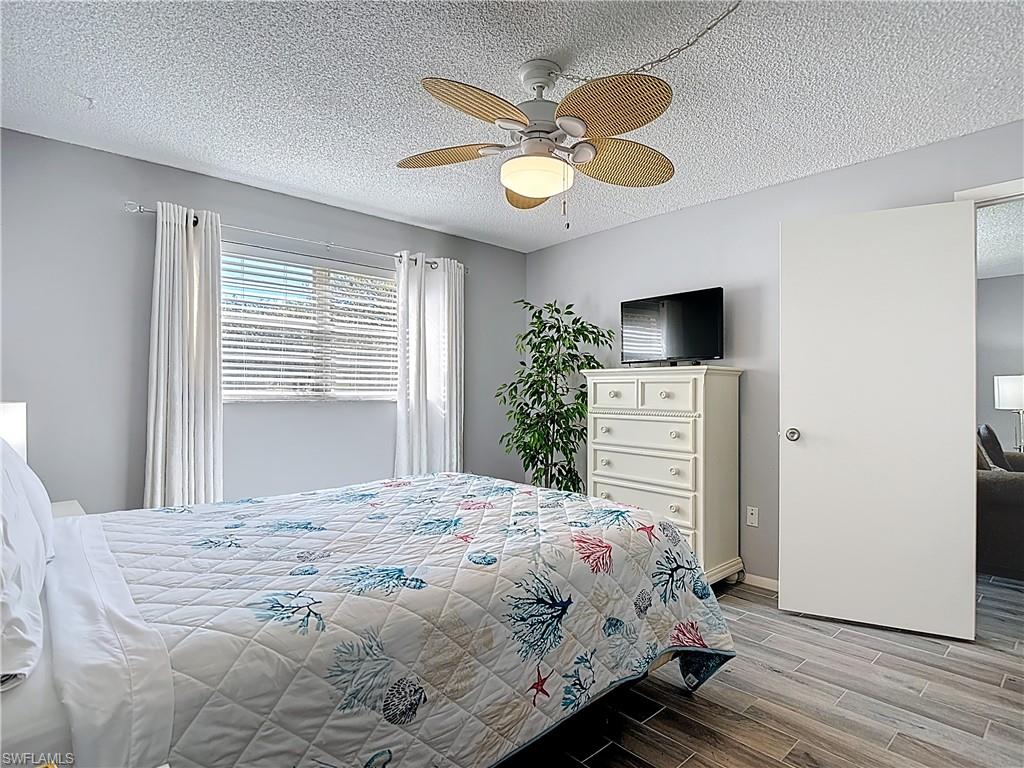 200 Turtle Lake Court, Unit 109 Naples, FL 34105 - Photo 25 of 37 Bedroom with a textured ceiling, wood finish floors, and a ceiling fan