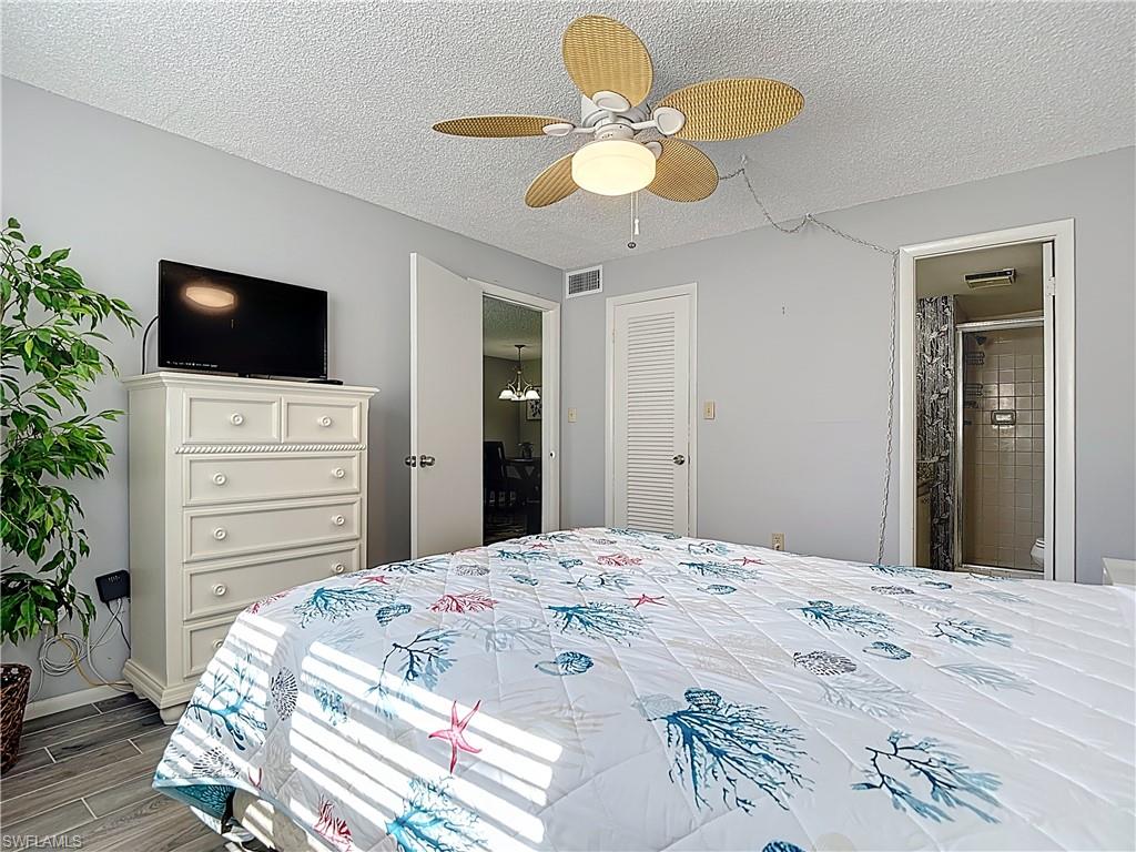 200 Turtle Lake Court, Unit 109 Naples, FL 34105 - Photo 28 of 37 Bedroom with a textured ceiling, wood tiled floors, ceiling fan, and connected bathroom