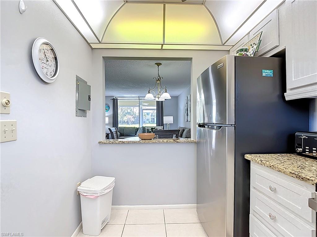 200 Turtle Lake Court, Unit 109 Naples, FL 34105 - Photo 5 of 37 Kitchen featuring light stone counters, light tile patterned floors, freestanding refrigerator, white cabinets, and a chandelier