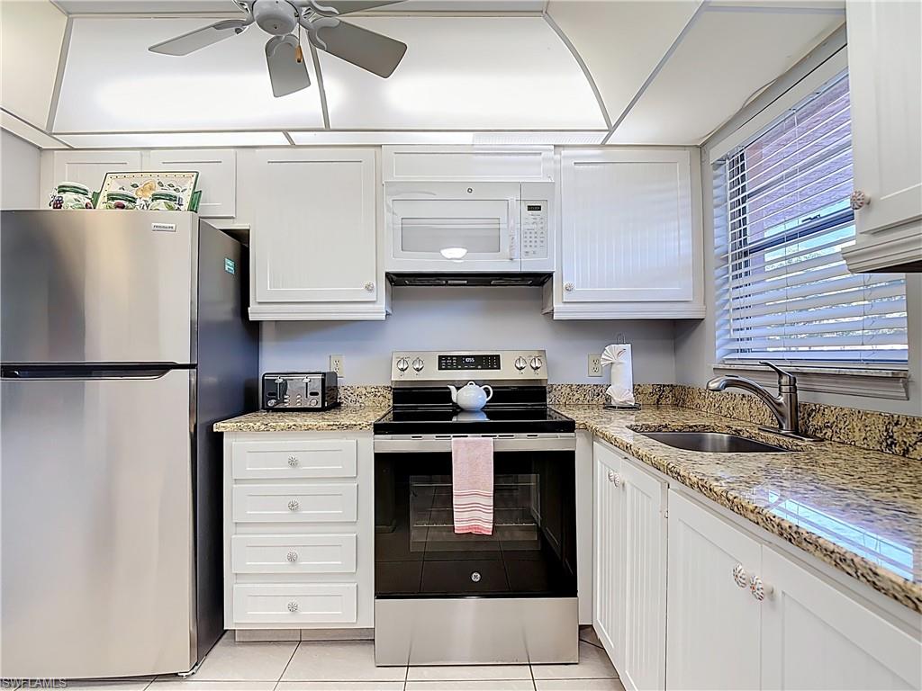 200 Turtle Lake Court, Unit 109 Naples, FL 34105 - Photo 7 of 37 Kitchen featuring appliances with stainless steel finishes, white cabinets, light stone countertops, light tile patterned floors, and a ceiling fan