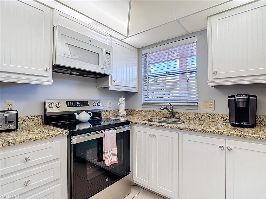 200 Turtle Lake Court, Unit 109 Naples, FL 34105 - Photo 8 of 37 Kitchen with stainless steel electric stove, white cabinets, white microwave, light stone countertops, and light tile patterned flooring