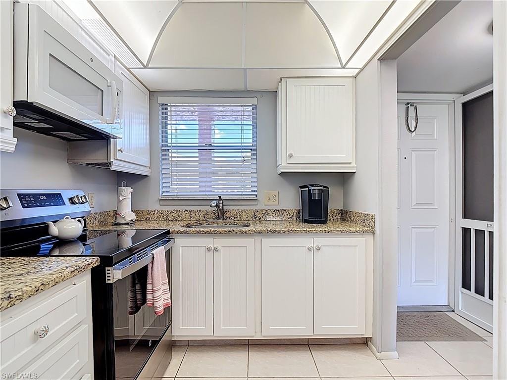 200 Turtle Lake Court, Unit 109 Naples, FL 34105 - Photo 9 of 37 Kitchen with electric stove, white microwave, white cabinets, light stone countertops, and light tile patterned floors
