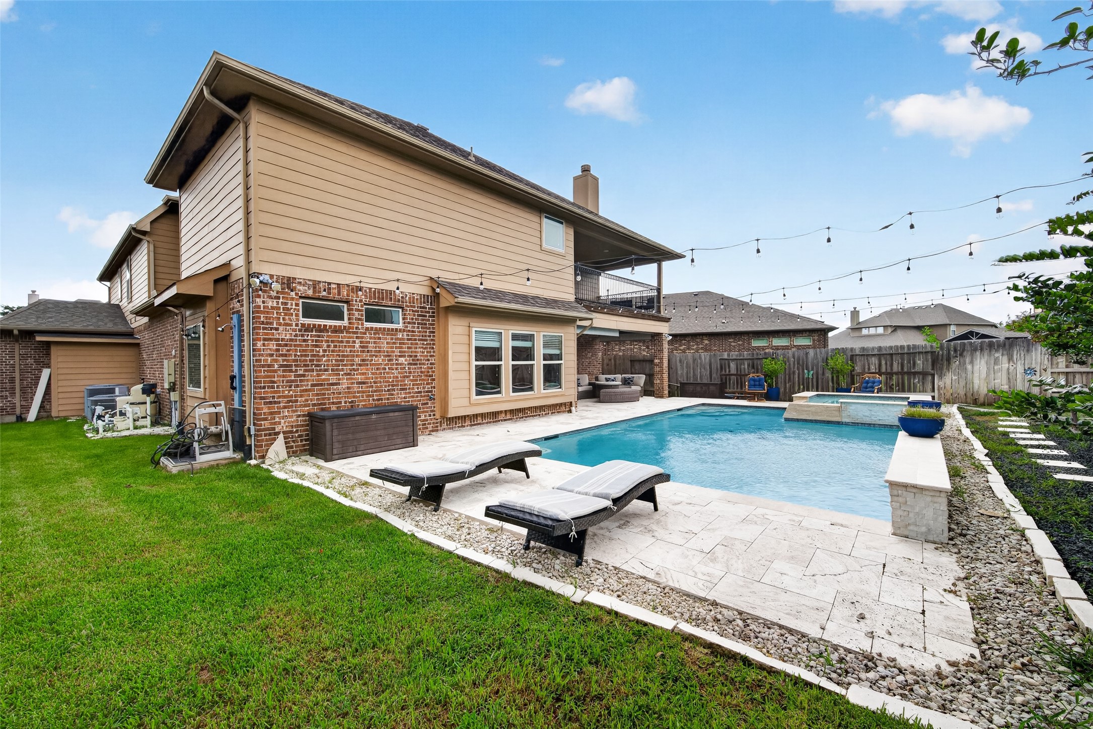 25611 Ellis Ridge Court Katy, TX 77494 - Photo 43 of 49 This photo showcases a spacious backyard featuring a modern two-story brick house with a wooden exterior. It includes a large swimming pool surrounded by a tiled patio, complete with lounge chairs. String lights add ambiance, and a well-maintained lawn enhances the outdoor space. Perfect for relaxation and entertaining.