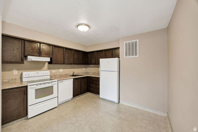 240 East 400 North, Unit 26 Logan, UT 84321 - Photo 2 of 12 Kitchen featuring dark wood-finish cabinetry, light-toned countertops, and an integrated white appliance package