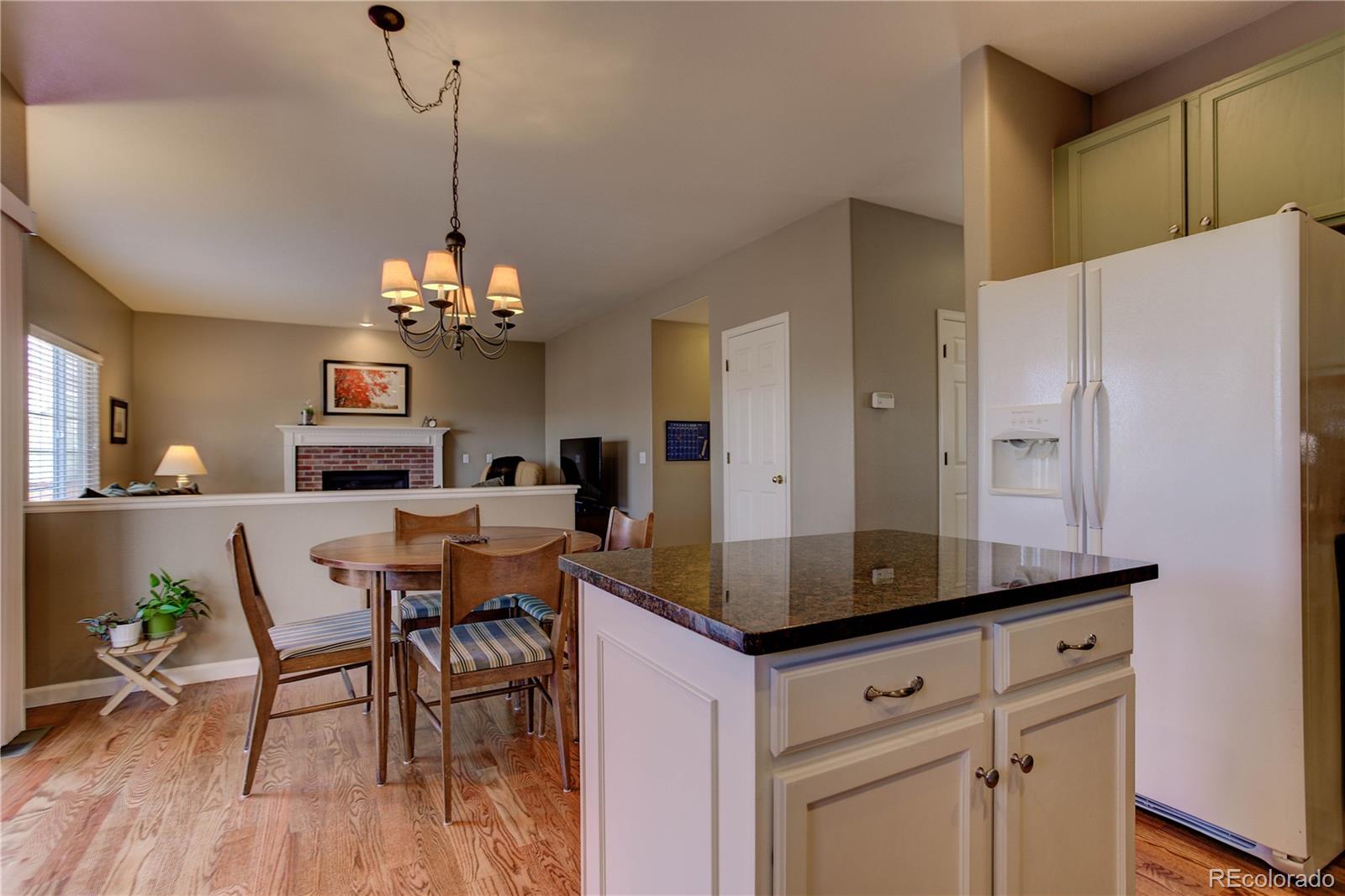 873 Riddlewood Lane Highlands Ranch, CO 80129 - Photo 9 of 35 a kitchen with stainless steel appliances granite countertop a stove a sink a refrigerator a dining table and chairs with wooden floor