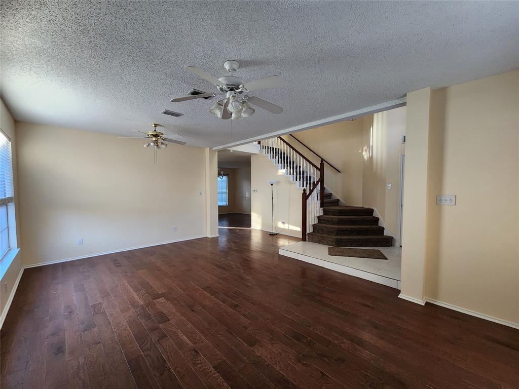2413 Timber Ridge Lane Flower Mound, TX 75028 - Photo 5 of 32 Spacious interior featuring rich wood-finish flooring, a carpeted staircase with white risers and wood banister, light cream wall paint, and multiple ceiling fans