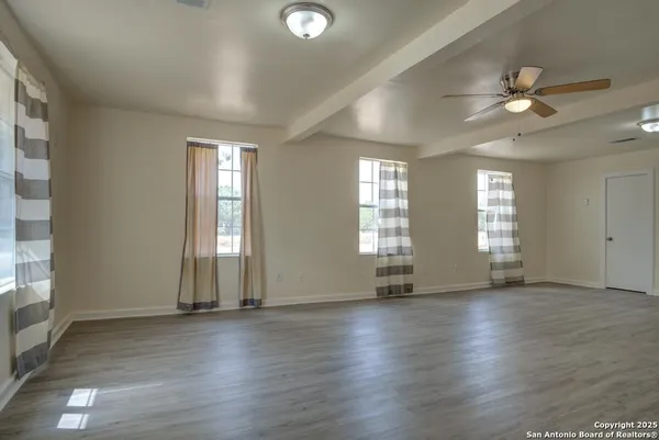 an empty room with wooden floor and windows with curtains