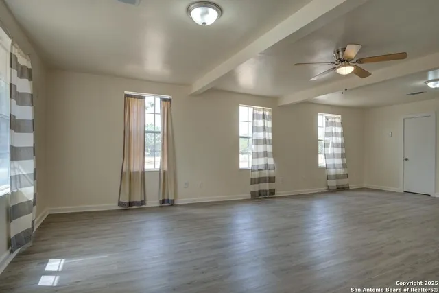 an empty room with wooden floor and windows with curtains