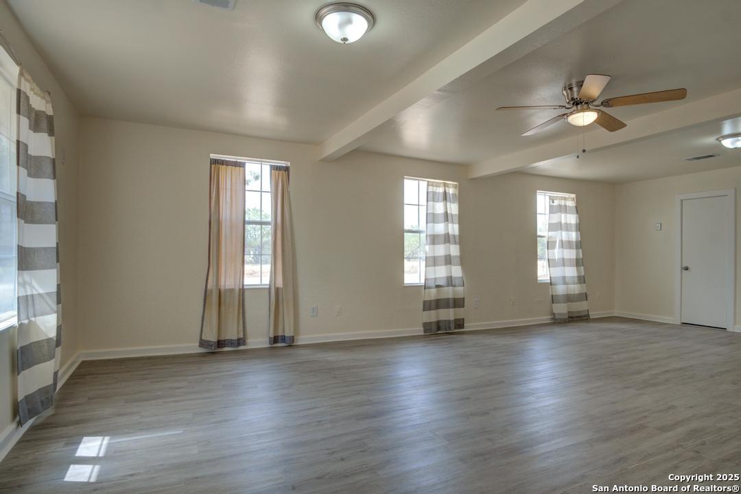 1176 Old Adams Lane Pleasanton, TX 78064 - Photo 6 of 42 an empty room with wooden floor and windows with curtains