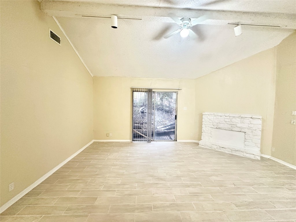 4302 Scottsdale Road, Unit B Austin, TX 78721 - Photo 15 of 37 Unfurnished living room featuring rail lighting, vaulted ceiling, a stone fireplace, a textured ceiling, and ceiling fan