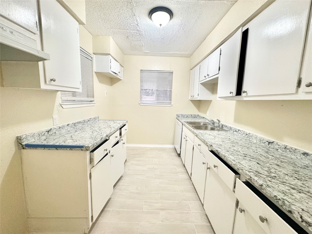 4302 Scottsdale Road, Unit B Austin, TX 78721 - Photo 10 of 37 Kitchen with a textured ceiling, under cabinet range hood, white cabinetry, dishwasher, and light stone countertops
