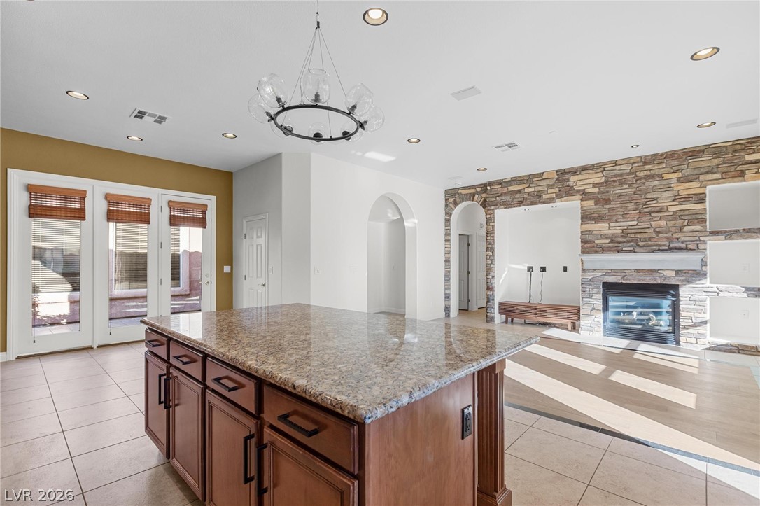11425 Rancho Portena Avenue Las Vegas, NV 89138 - Photo 57 of 58 Kitchen featuring arched walkways, light stone counters, a center island, a stone fireplace, and open floor plan