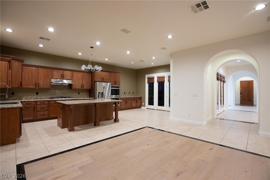 11425 Rancho Portena Avenue Las Vegas, NV 89138 - Photo 29 of 58 Kitchen featuring arched walkways, light wood-type flooring, a kitchen bar, light stone counters, and a kitchen island