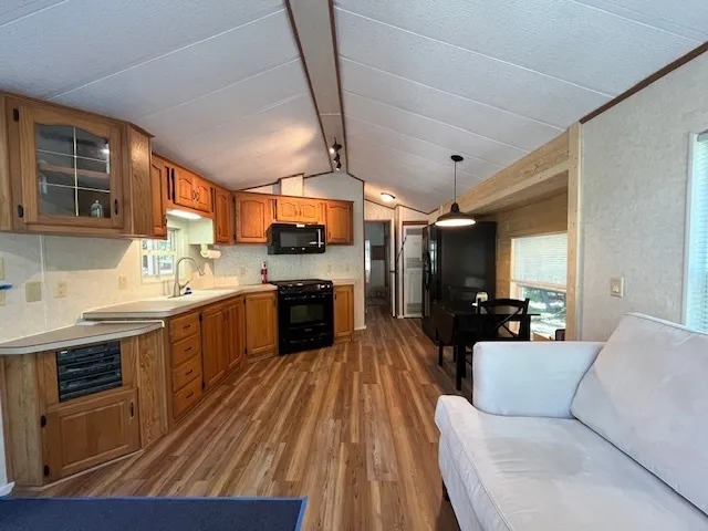 a living room with stainless steel appliances kitchen island granite countertop a stove a sink dishwasher a microwave oven and a dining table with wooden floor