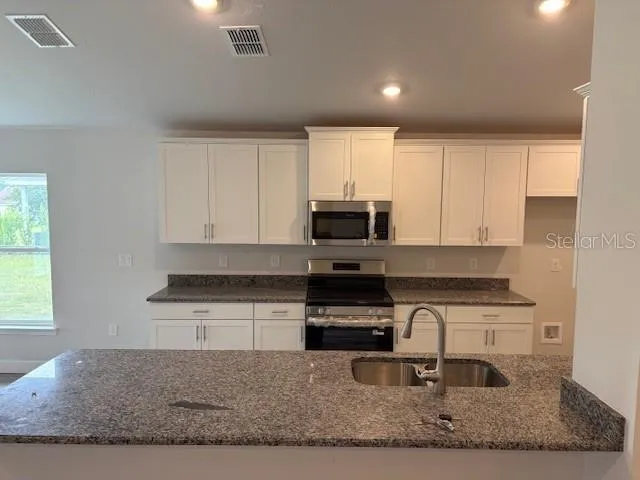 a kitchen with stainless steel appliances granite countertop a stove a sink and a microwave