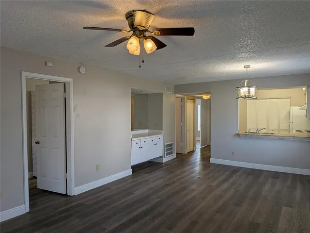 an empty room with wooden floor chandelier ceiling fan and windows