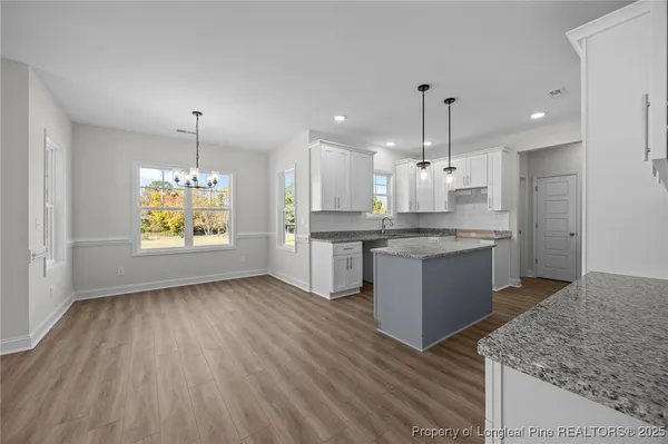 a white kitchen with granite countertop a stove top oven a sink dishwasher a refrigerator and white cabinets with wooden floor