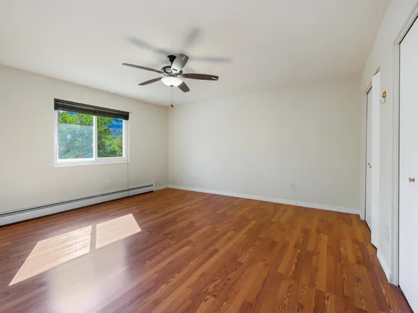 a view of empty room with wooden floor and fan