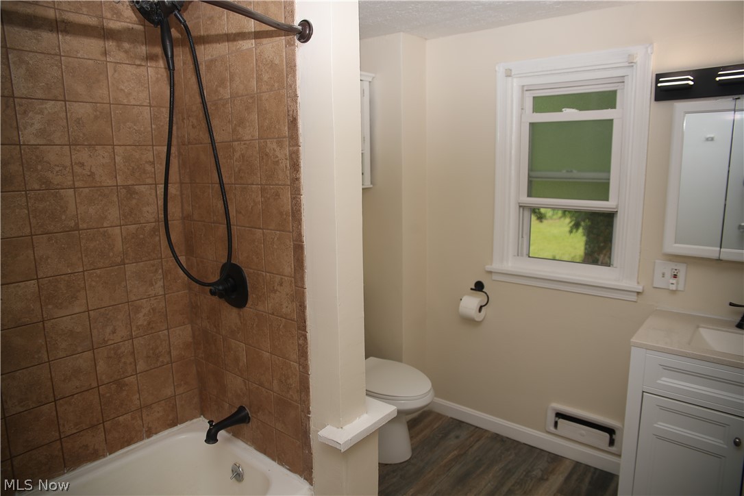 1087 Krumroy Road Akron, OH 44306 - Photo 22 of 23 Bathroom featuring a tiled shower surround with a tub, a white vanity with a light-colored countertop, and wood-finish flooring