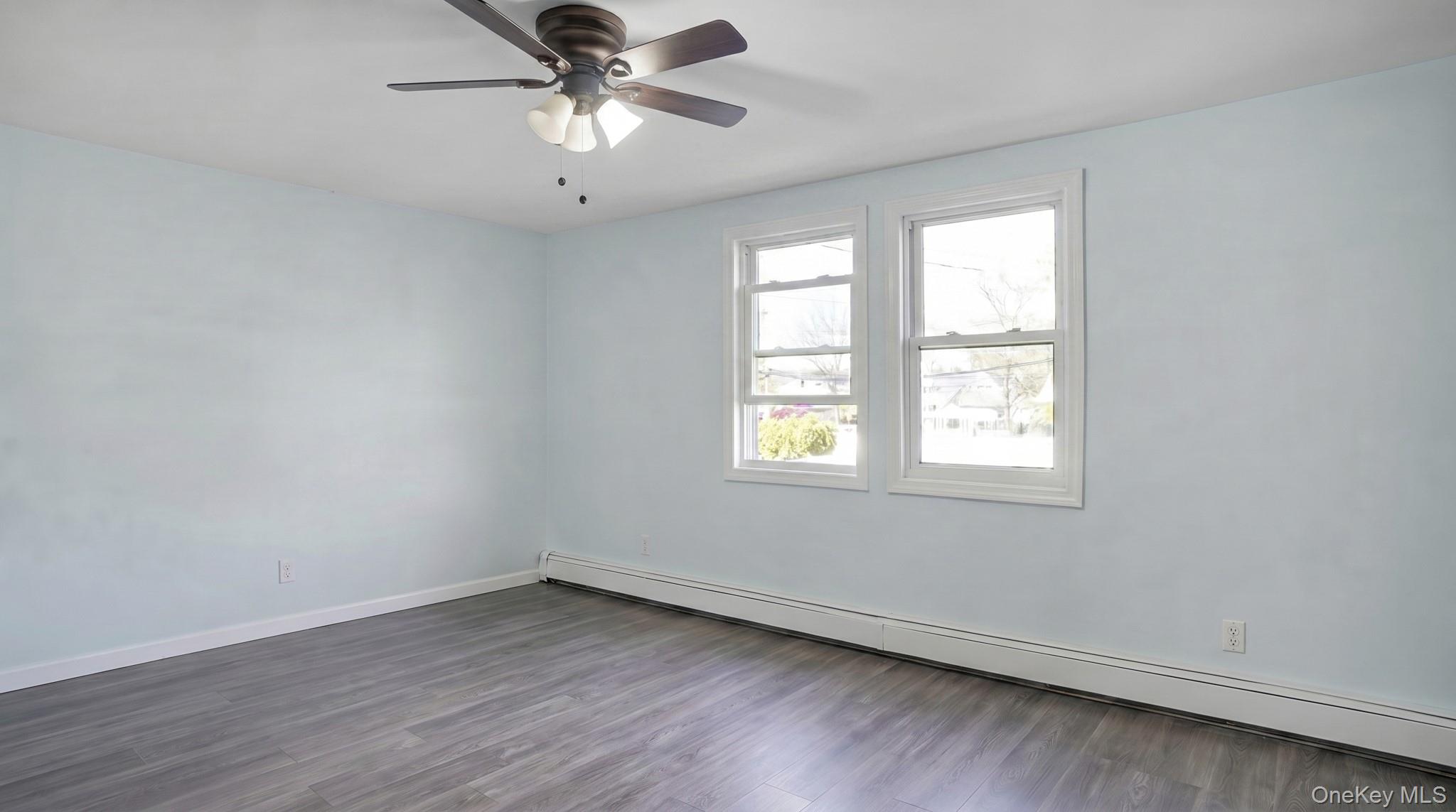 63 Blacksmith Road Levittown, NY 11756 - Photo 19 of 25 Spacious room featuring wood-finish flooring, two large windows, a ceiling fan with integrated lighting, and baseboard heating