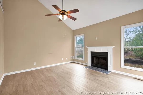 an empty room with windows fireplace and a ceiling fan