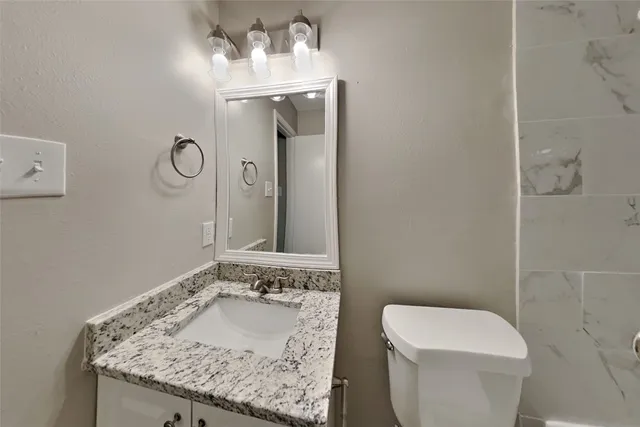 a bathroom with a granite countertop sink a toilet and a mirror
