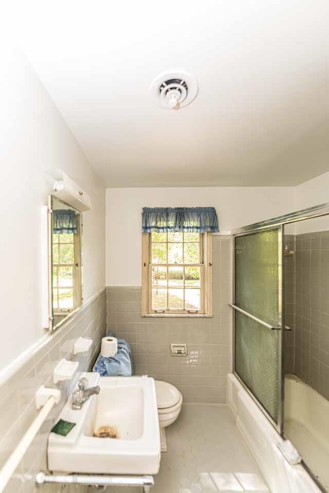 5575 Walnut Grove Road Memphis, TN 38120 - Photo 34 of 36 Full bathroom with tile walls, shower / bath combination with glass door, wainscoting, and tile patterned flooring