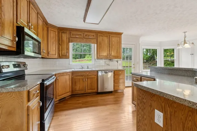 a kitchen with stainless steel appliances granite countertop wooden cabinets a sink a stove a window and island