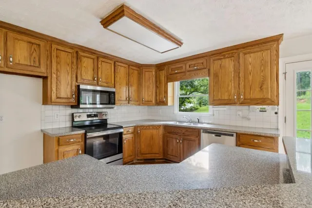 a kitchen with stainless steel appliances granite countertop a sink a stove cabinets counter space and a window