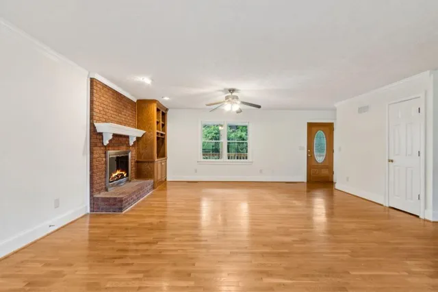 an empty room with wooden floor fireplace and windows