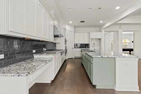 a large kitchen with stainless steel appliances granite countertop a stove a sink a refrigerator and white cabinets