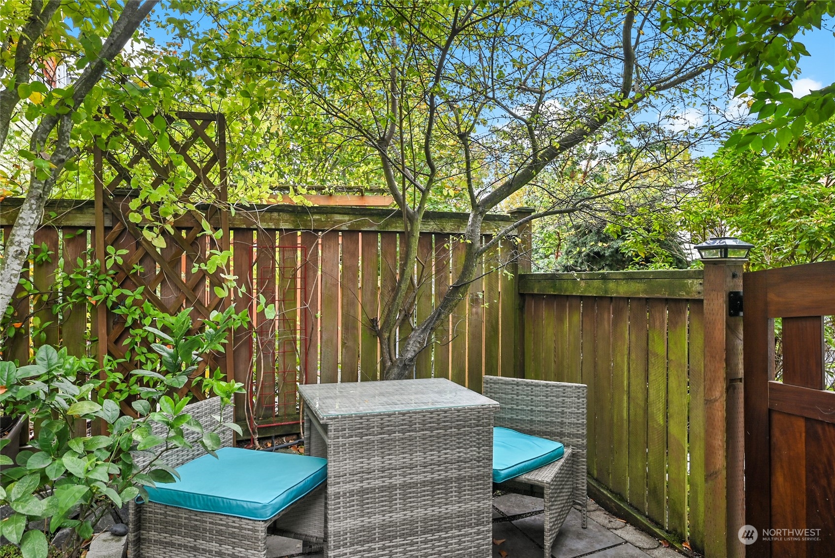 4408 Meridian Avenue North, Unit A Seattle, WA 98103 - Photo 25 of 31 a wooden bench sitting in backside of a house with potted plants and large trees