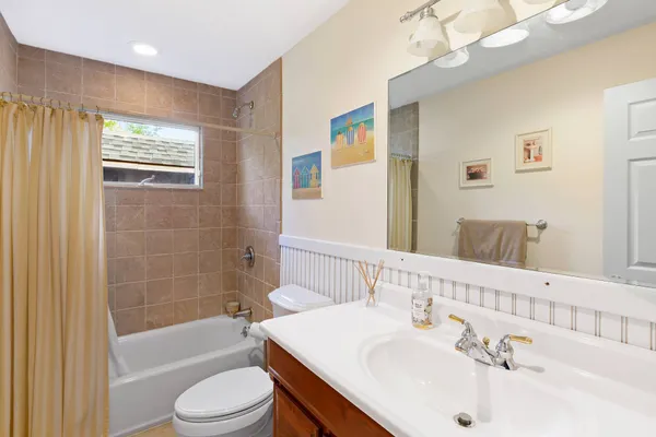 a bathroom with a bathtub shower sink vanity mirror and toilet