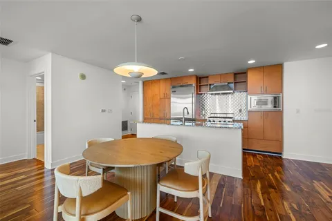 a kitchen with stainless steel appliances kitchen island granite countertop a dining table chairs and a refrigerator